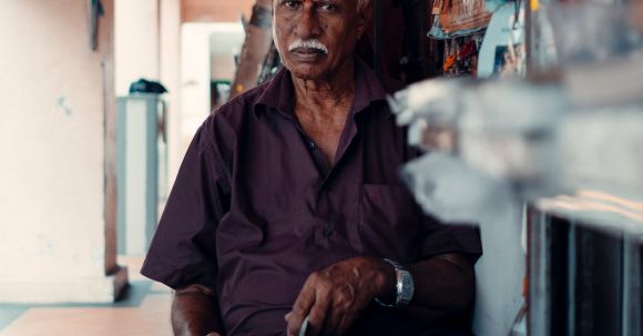 Local Immersion - Serious elderly Indian male in shirt sitting in street market with magazines while looking at camera in daylight