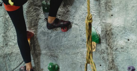 Balance, Coordination - Crop anonymous risky female with belaying equipment training on stony gray climbing wall