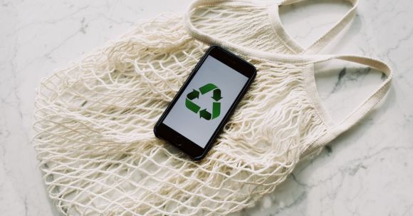 Sustainable Fashion: Reducing Impact - Overhead of smartphone with simple recycling sign on screen placed on white eco friendly mesh bag on marble table in room