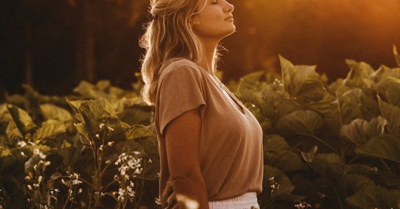 Positive Mindset, Abundance. - Side view attractive young female in casual summer wear standing with eyes closed on abundant field in peaceful countryside at sunset