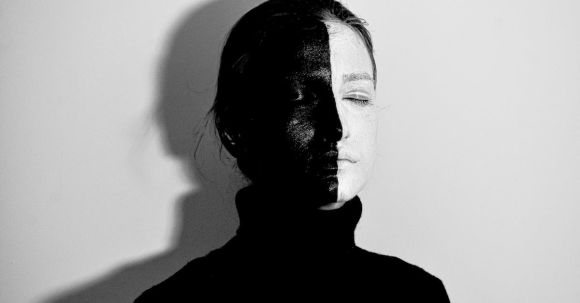Color Psychology - Black and white of woman with face painted in white and black colors standing with closed eyes against light wall with shadow