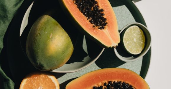 Ingredient Roles - Top view of halves of ripe papaya together with oranges and limes placed on green round dishes and green fabric on white background
