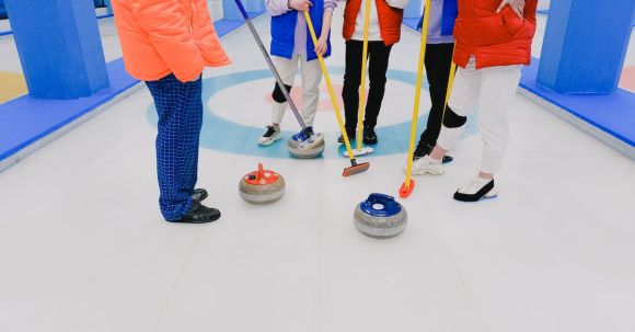 Olympic Training - Crop players of curling professional team in sportswear with brooms and stones standing on ice rink